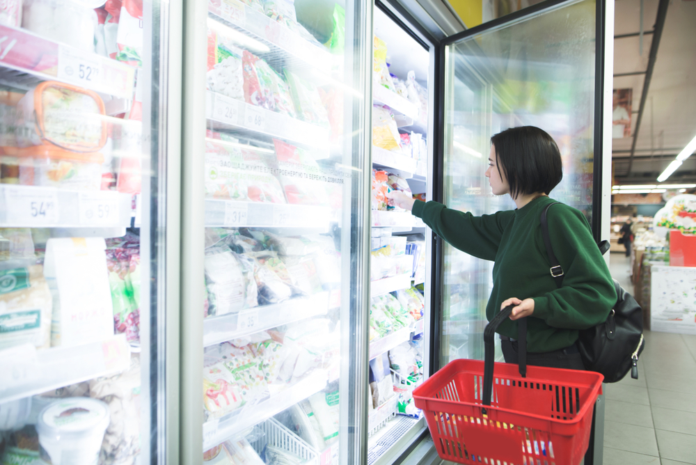 Woman picks food item from freezer in supermarket.